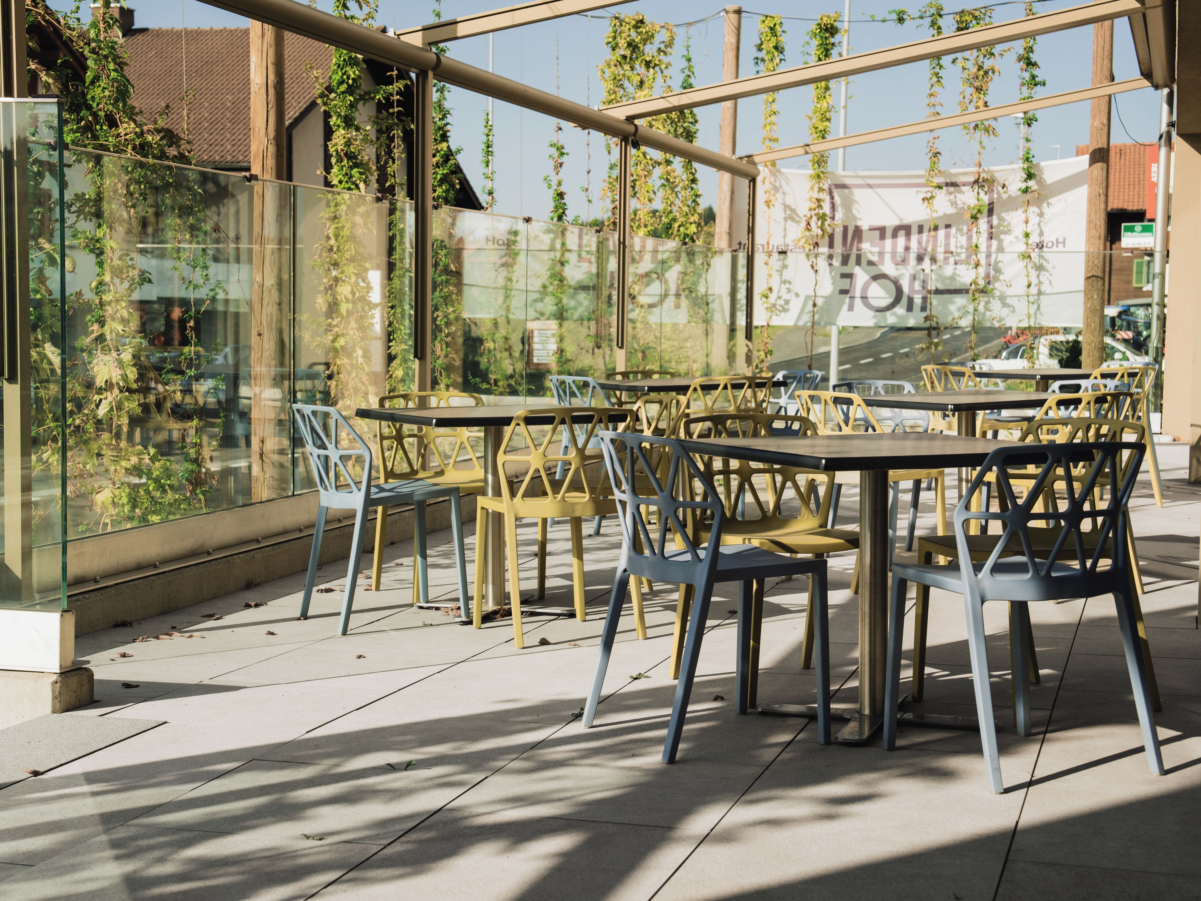 An outdoor seating area with tables and chairs, surrounded by glass walls with greenery.
