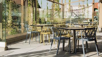 An outdoor seating area with tables and chairs, surrounded by glass walls with greenery.