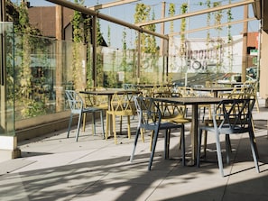 An outdoor seating area with tables and chairs, surrounded by glass walls with greenery. - Hotel Lindenhof (Entlebuch)
