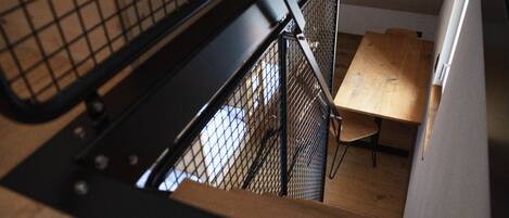 A staircase with a metal railing leading to a room with a wooden table and a chair.