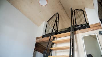 Ett rum i loftstil med ett träbeklätt tak, en metallstege och en dörr som leder till ett annat utrymme.