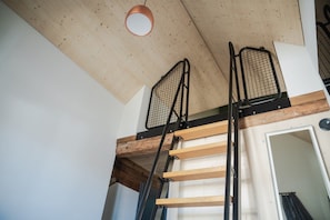 A loft-style room with a wooden ceiling, a metal ladder, and a door leading to another space. - Hotel Lindenhof (Entlebuch)