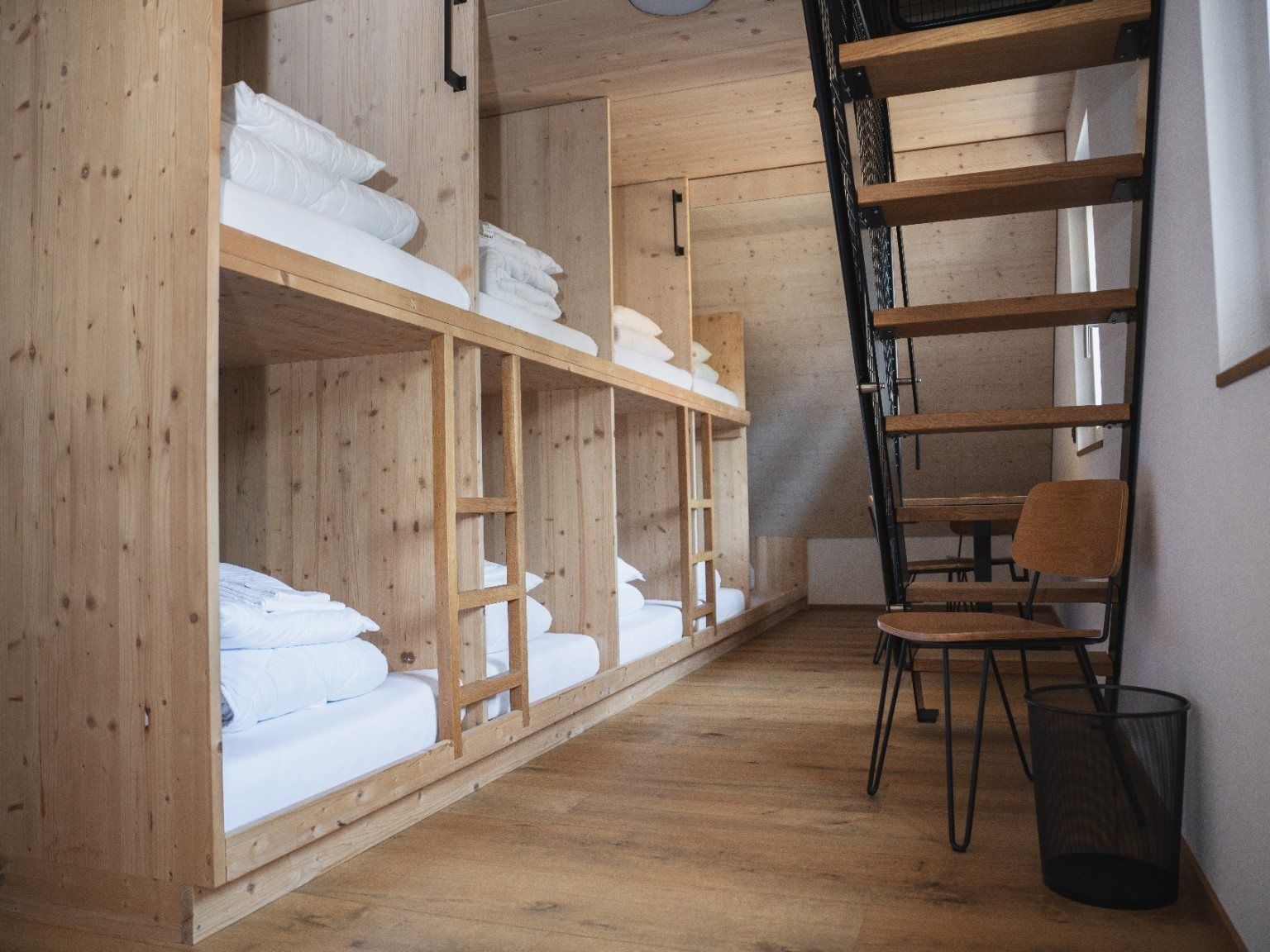 A room with wooden bunk beds, a desk, and a chair.