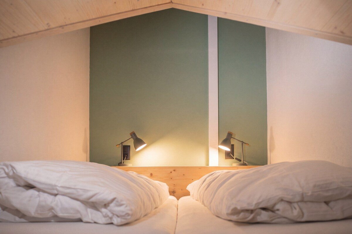 Una habitación con dos camas, cada una con ropa blanca y dos lámparas de noche.