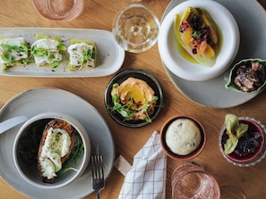 Variedad de platos sobre una mesa de madera, incluyendo un tazón de sopa, un plato con ensalada verde y un recipiente con huevo escalfado.