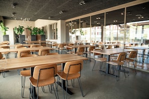 A spacious indoor dining area with multiple wooden tables and chairs, large windows allowing natural light, and potted plants. - Hotel Lindenhof (Entlebuch)
