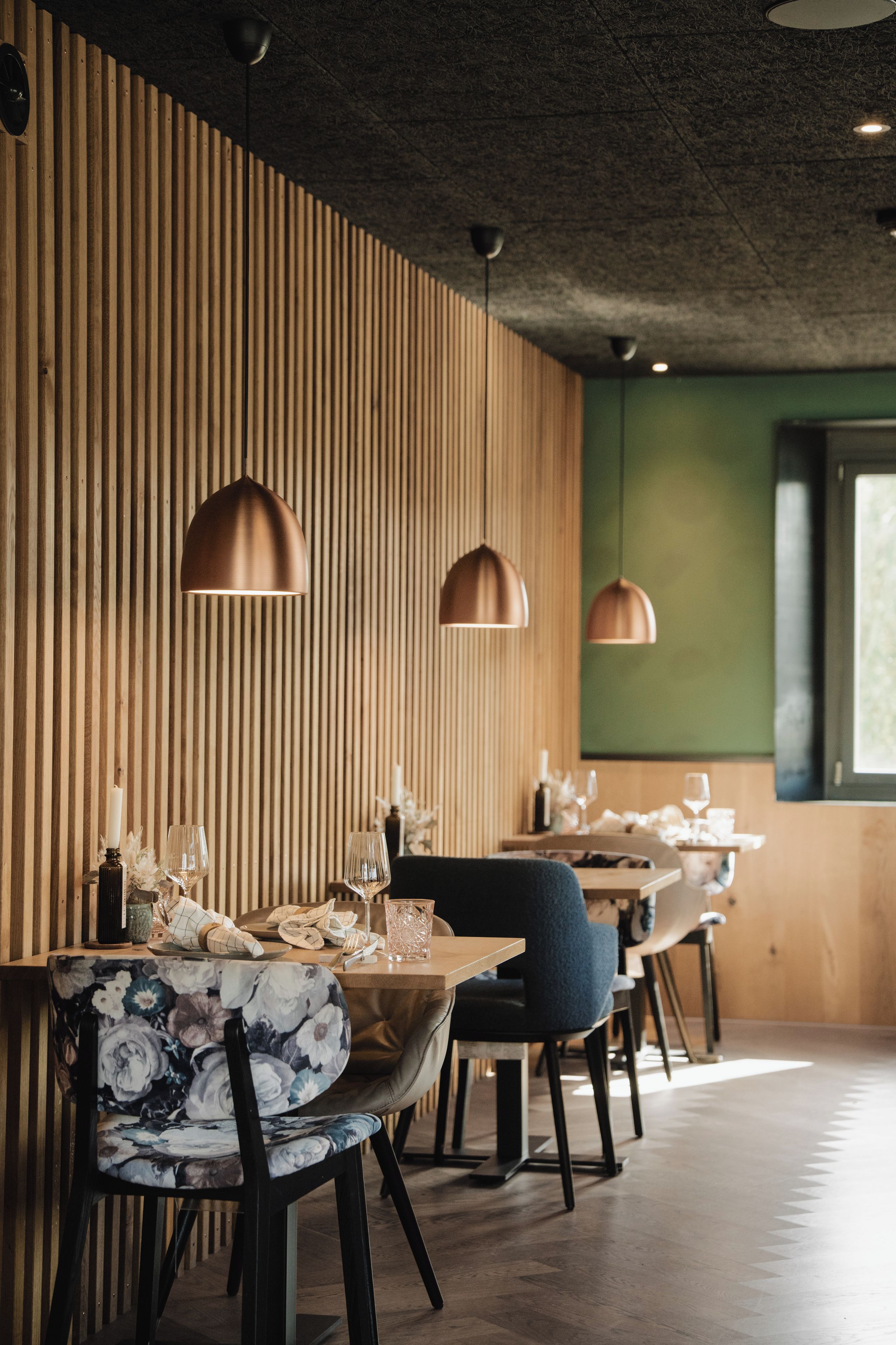 A restaurant interior with wooden panel walls, pendant lighting, and a dining area with tables and chairs.