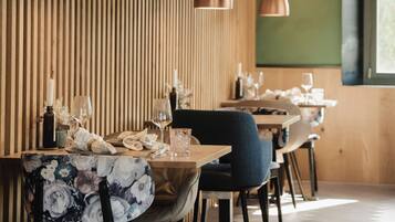 A restaurant interior with wooden panel walls, pendant lighting, and a dining area with tables and chairs.