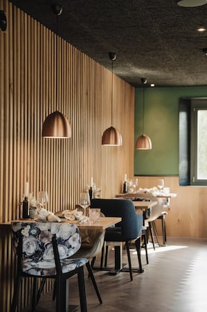 A restaurant interior with wooden panel walls, pendant lighting, and a dining area with tables and chairs. - Hotel Lindenhof (Entlebuch)