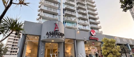 Un hotel de gran altura con una entrada destacada, un número de dirección visible y un letrero que anuncia un salón de belleza cercano.