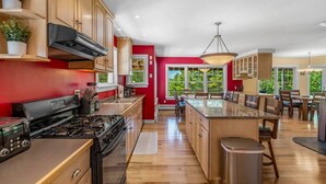 A kitchen with wooden cabinets, a gas stove, and a large island with seating. - 5BR Home Quietside of MDI - Sleeps 23! [Headlands] (Tremont)