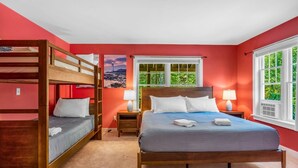 A bedroom with a bunk bed, a double bed, two bedside tables with lamps, a window with a view of greenery, and a painting on the wall. - 5BR Home Quietside of MDI - Sleeps 23! [Headlands] (Tremont)