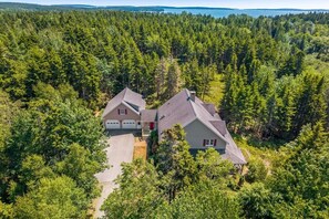 A two-story house with a garage, surrounded by dense forest. - 5BR Home Quietside of MDI - Sleeps 23! [Headlands] (Tremont)
