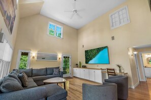 Ein geräumiges Wohnzimmer mit grauem Sofa, einem Couchtisch und einem an der Wand befestigten Fernseher.