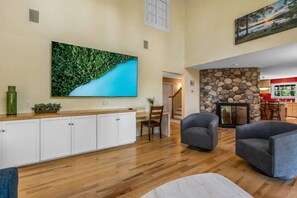 A spacious living room with a wooden floor, a stone fireplace, and a large green wall art piece. - 5BR Home Quietside of MDI - Sleeps 23! [Headlands] (Tremont)