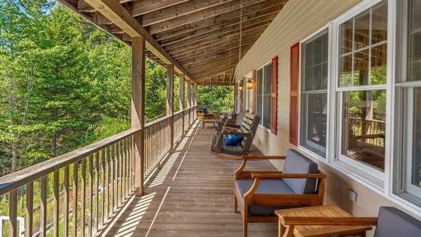 A wooden deck with outdoor furniture, large windows, and a view of a forested area. - 5BR Home Quietside of MDI - Sleeps 23! [Headlands] (Tremont)