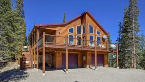 Una baita di legno a due piani con un balcone, diverse finestre e un vialetto sterrato.