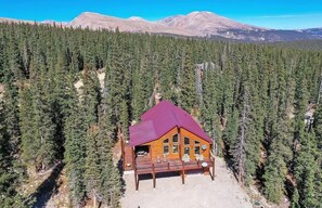 Eine Lodge mit rotem Dach, umgeben von dichtem Wald und Bergen im Hintergrund.