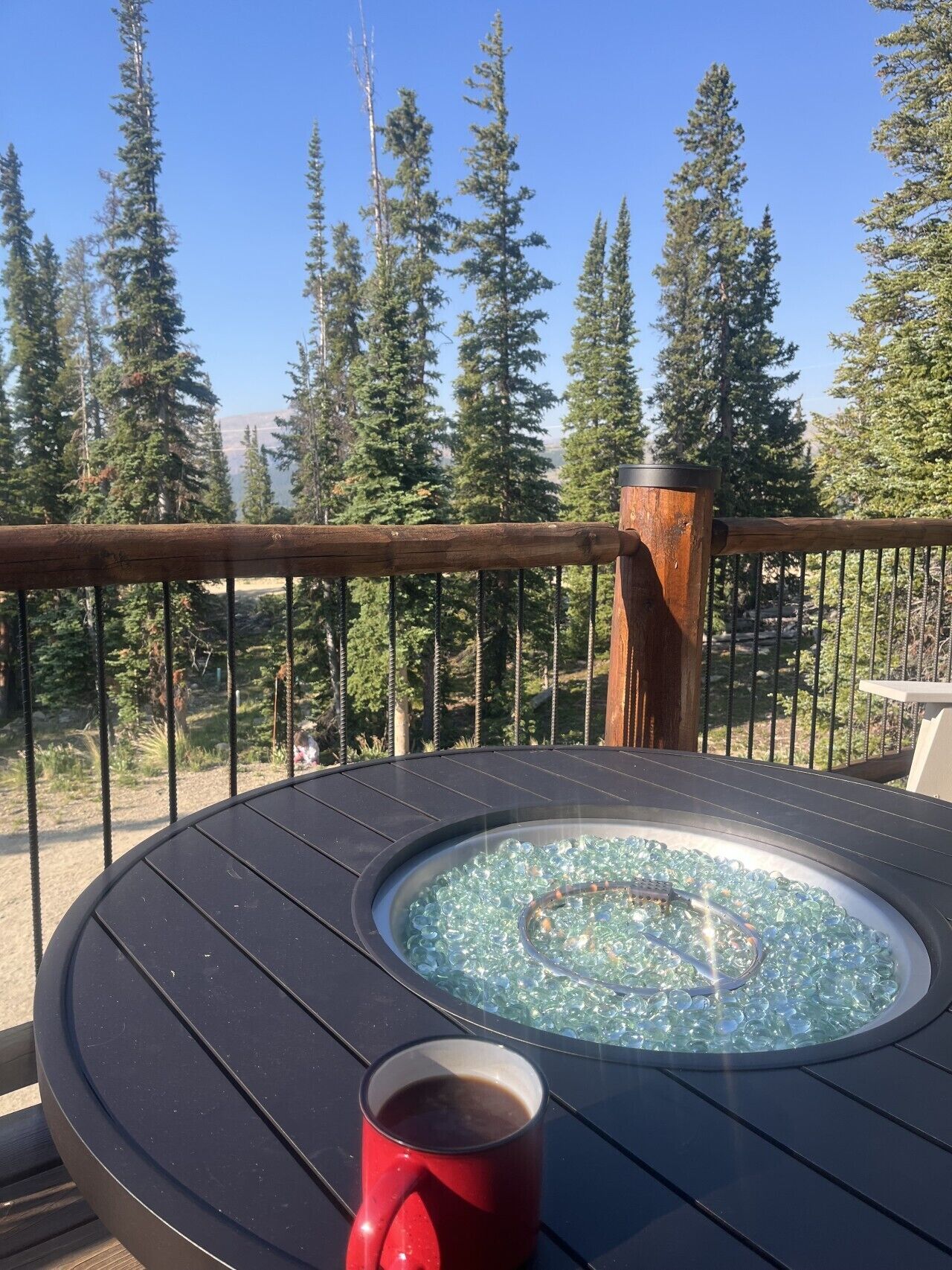 Une table ronde avec un plateau en verre et une tasse rouge, posée sur un balcon d’où l’on peut admirer de grands arbres.