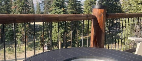 A round table with a glass top and a red mug, set on a balcony with a view of tall trees.