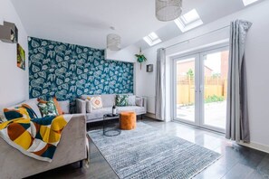 A modern living room with a sofa, a coffee table, a patterned wall, and a view through a sliding glass door. - Huge 4BR 2.5BT Home - Pool Table - Etihad - COOP (Greater Manchester)