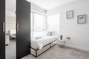 A modern bedroom with a bed, two windows, a bedside table, and a wall with two framed pictures. - Huge 4BR 2.5BT Home - Pool Table - Etihad - COOP (Greater Manchester)