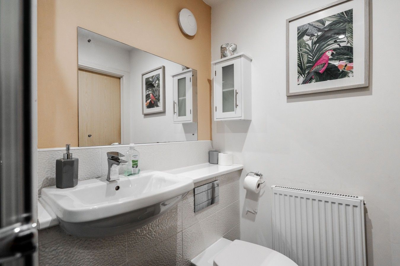 Ein Badezimmer mit weißem Waschbecken, Spiegel, Toilette und Handtuchheizkörper.