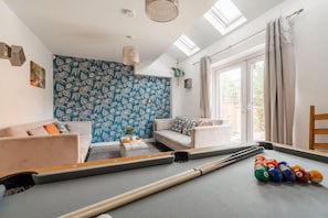 Ein Wohnzimmer mit Billardtisch, zwei Sofas, einem kleinen Couchtisch und einem großen Fenster mit Vorhängen.
