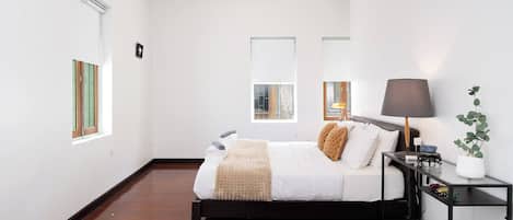 Um quarto moderno com cama, mesa de cabeceira, luminária e um vaso de planta.