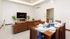 A modern living room with a flat-screen TV, a sofa, a dining table set for four, and a ceiling light fixture. - Spacious Heritage House Prime Location Family Stay (Bangkok)