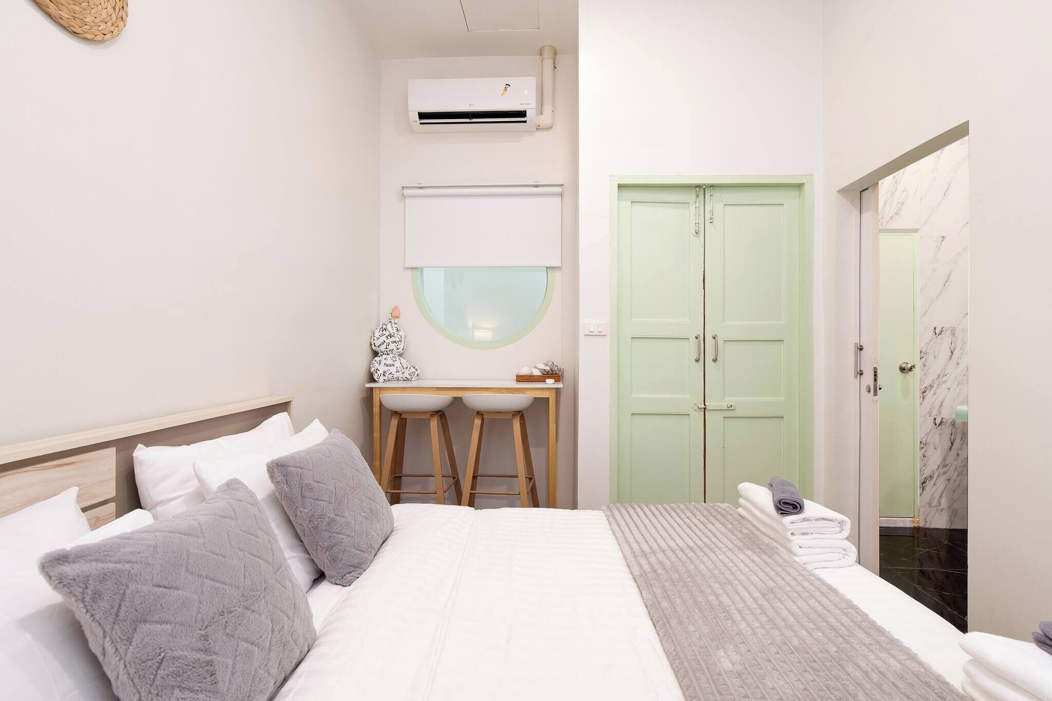Un dormitorio con cama, mesitas de noche, escritorio, aire acondicionado, puerta verde y baño con piso de mármol.