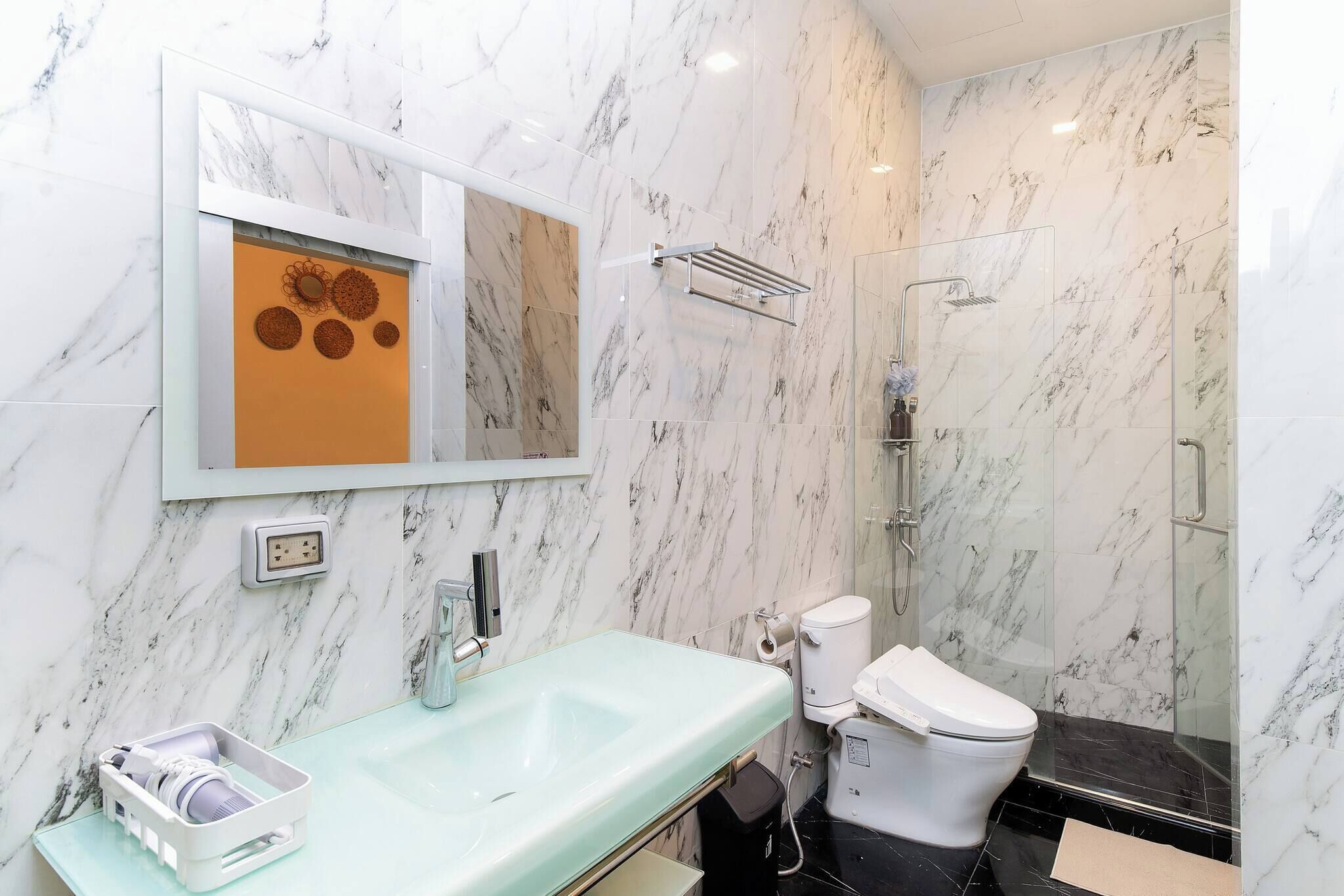 A bathroom with a marble wall, a glass sink, a toilet, and a shower.