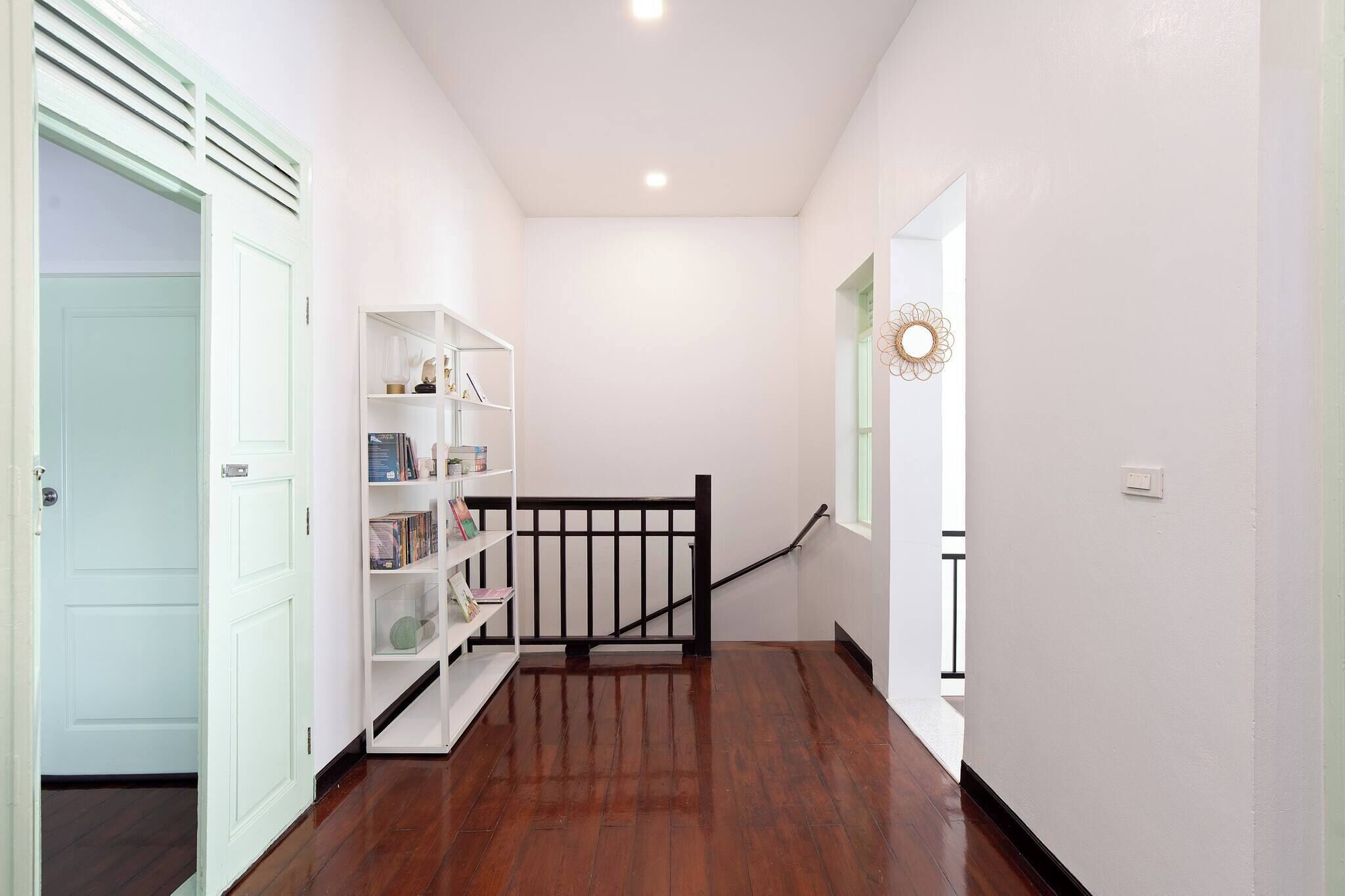 A hallway with a wooden floor, a white bookshelf, and a black railing.