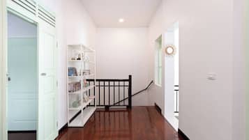 A hallway with a wooden floor, a white bookshelf, and a black railing.