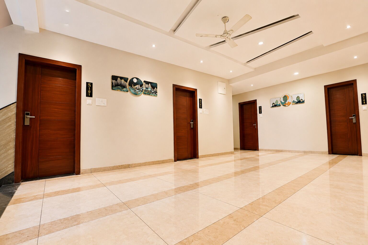 Corredor de hotel com portas de madeira, ventilador de teto e obras de arte nas paredes.