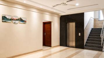 A hotel lobby with a marble floor, a wooden door, an elevator, and a staircase with metal railings.