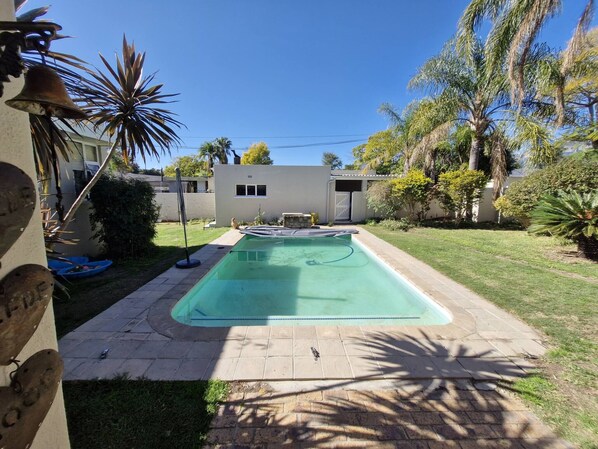 A swimming pool with a tiled deck, surrounded by a grassy yard and palm trees.