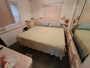 A bedroom with a single bed, bedside tables, a dresser, a window with blinds, and a small table with a plate and utensils. - Cozy ICWW waterfront 2-bedroom cottage in soothing Myrtle Beach (Myrtle Beach)