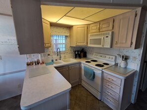 A compact kitchen with a microwave, stove, sink, and cabinets. - Cozy ICWW waterfront 2-bedroom cottage in soothing Myrtle Beach (Myrtle Beach)