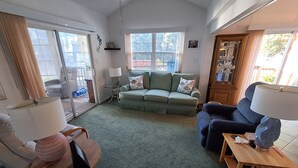 A living room with a green sofa, a blue armchair, a small table, and a lamp. - Cozy ICWW waterfront 2-bedroom cottage in soothing Myrtle Beach (Myrtle Beach)