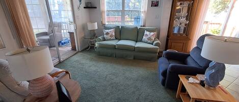 Un salon avec un canapé vert, un fauteuil bleu, une petite table et une lampe.