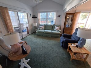 A living room with a green sofa, a blue armchair, a small table, and a lamp. - Cozy ICWW waterfront 2-bedroom cottage in soothing Myrtle Beach (Myrtle Beach)