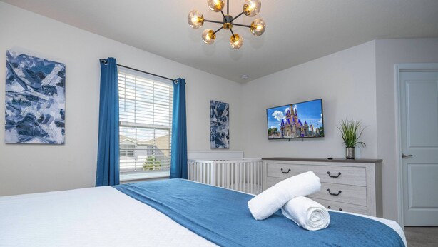 A hotel room with a bed, a television, artwork, a window with curtains, and a radiator. - Stunning Windsor Island 10BR (Davenport)