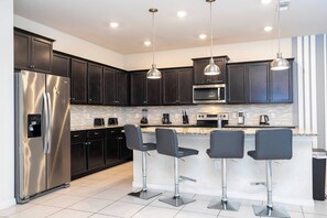 Uma cozinha moderna com armários escuros, eletrodomésticos de aço inoxidável, uma ilha central com banquetas e iluminação pendente.