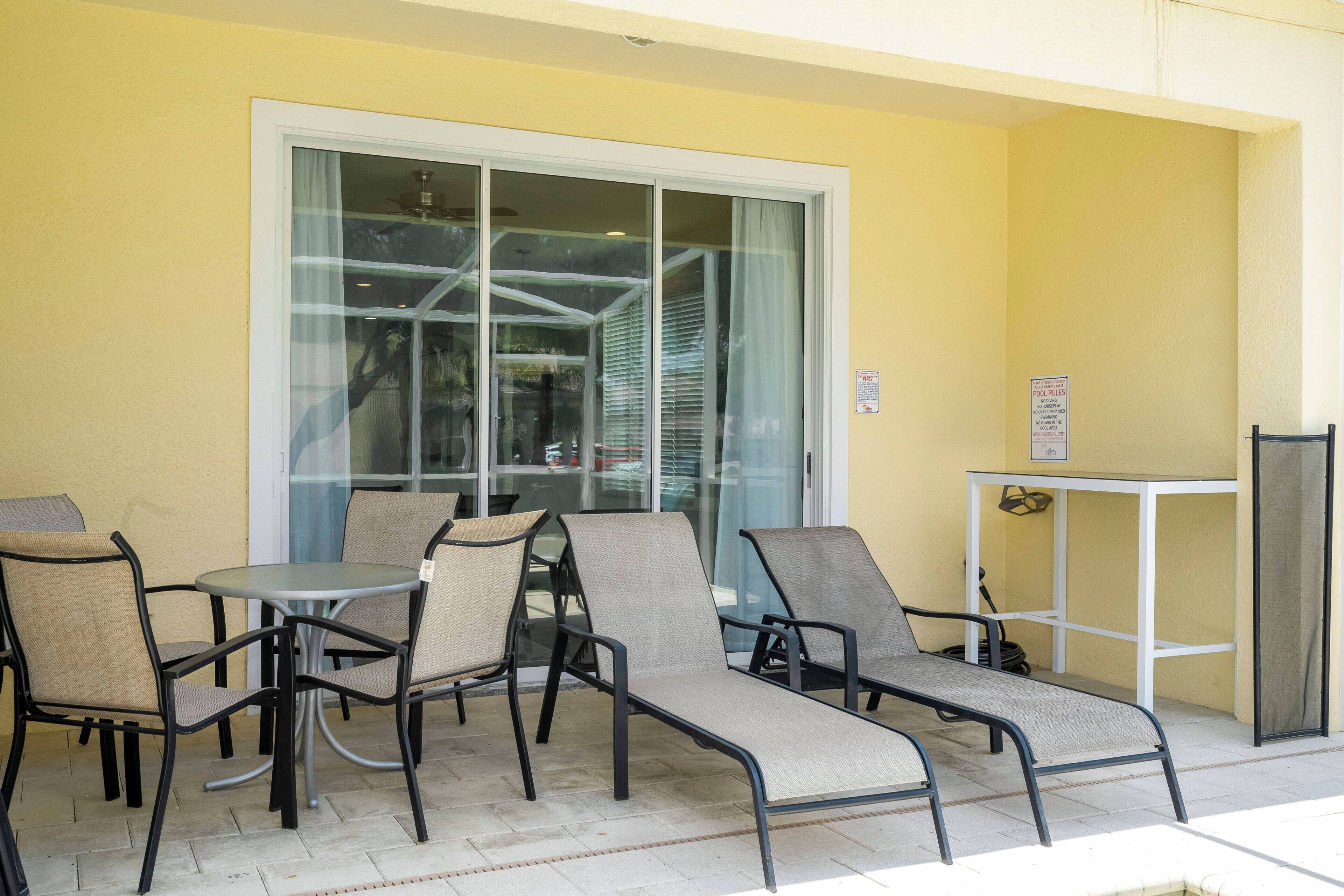 An outdoor seating area with chairs and tables, a glass door, and a pool safety sign.