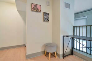 A corner of a room with a grey upholstered stool, a black metal table, and two framed artworks on the wall. - Chic City Loft - Nearby Parking - Hospitals - 2F (Louisville)