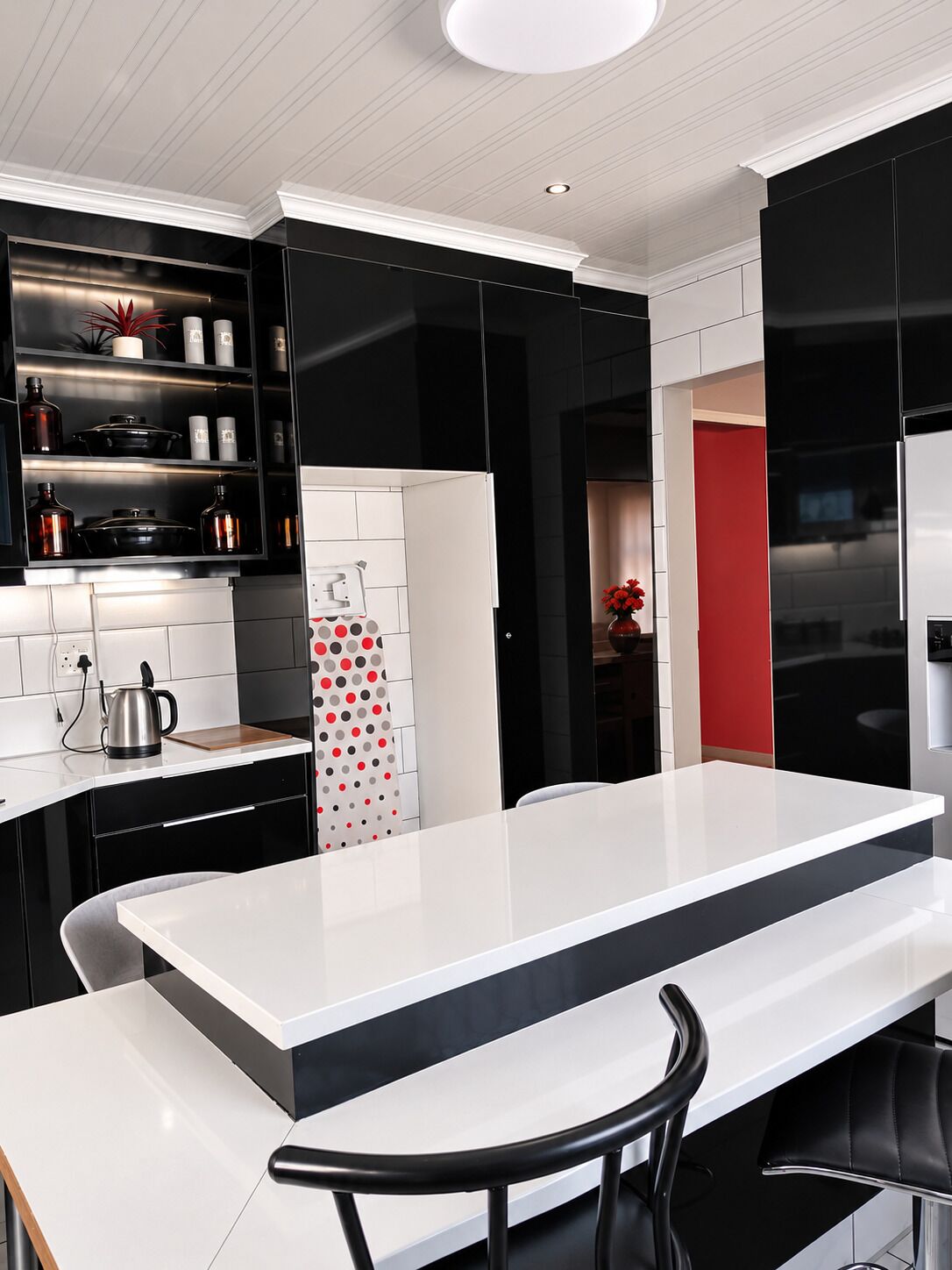 A modern kitchen with black cabinets, a white countertop, and a red accent wall.