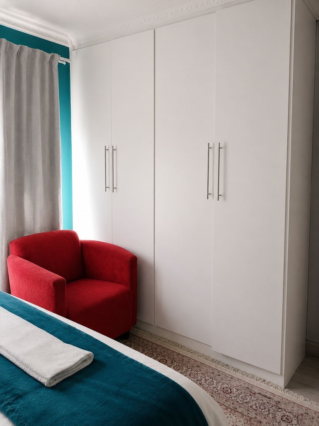 A bedroom with a bed, a red chair, and a wardrobe.