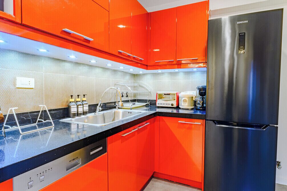 A kitchen with red cabinets, a stainless steel refrigerator, and a black countertop.