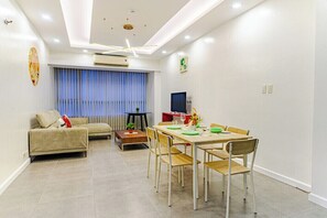 A modern living room with a sofa, dining table, and chairs. There is a TV on the wall and a window with curtains. - Relaxing Condo Stay in Seibu Tower (Taguig City)